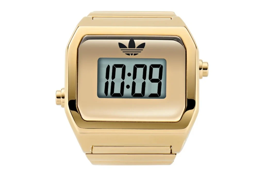 Front view of a gold-tone adidas Digital Two ring watch with LCD display and trefoil logo on white background.
