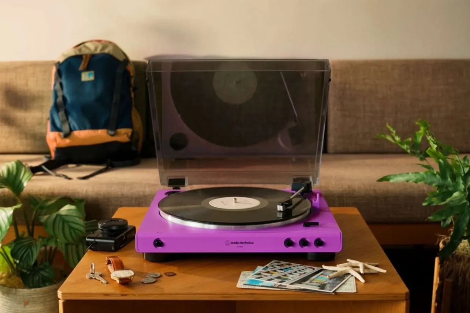 Purple Audio-Technica AT-LP60XBT turntable playing a record on a wooden table with dust cover open, lifestyle scene with sof…