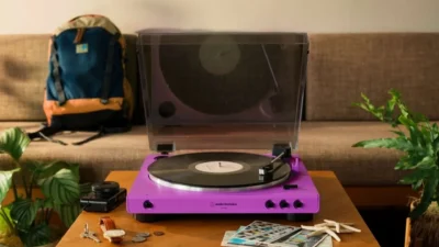 Purple Audio-Technica AT-LP60XBT turntable playing a record on a wooden table with dust cover open, lifestyle scene with sof…