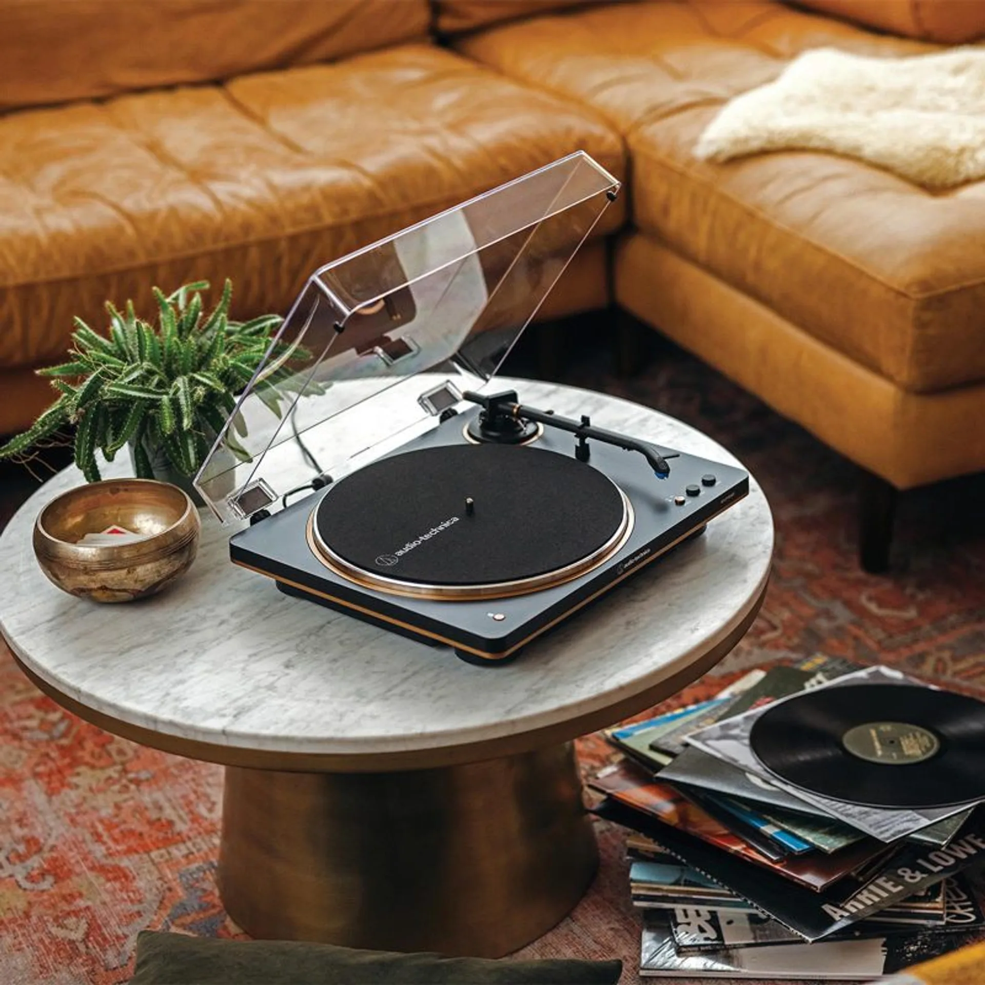 Audio-Technica AT-LP70XBT turntable with gold trim and open dust cover on a round marble coffee table in a warm living room…