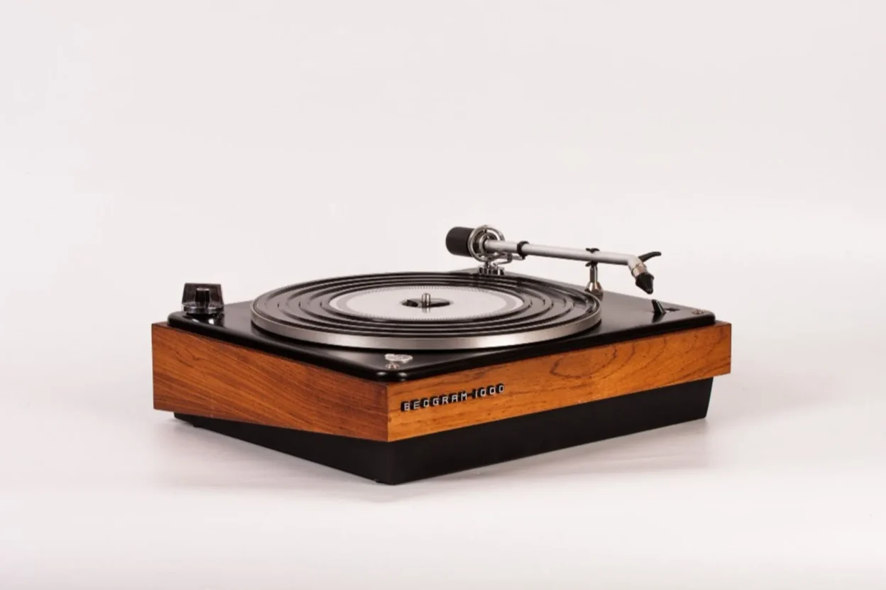 Close-up of Beogram 1000 silver tonearm over platter with black rubber mat and wood base, shallow depth of field.