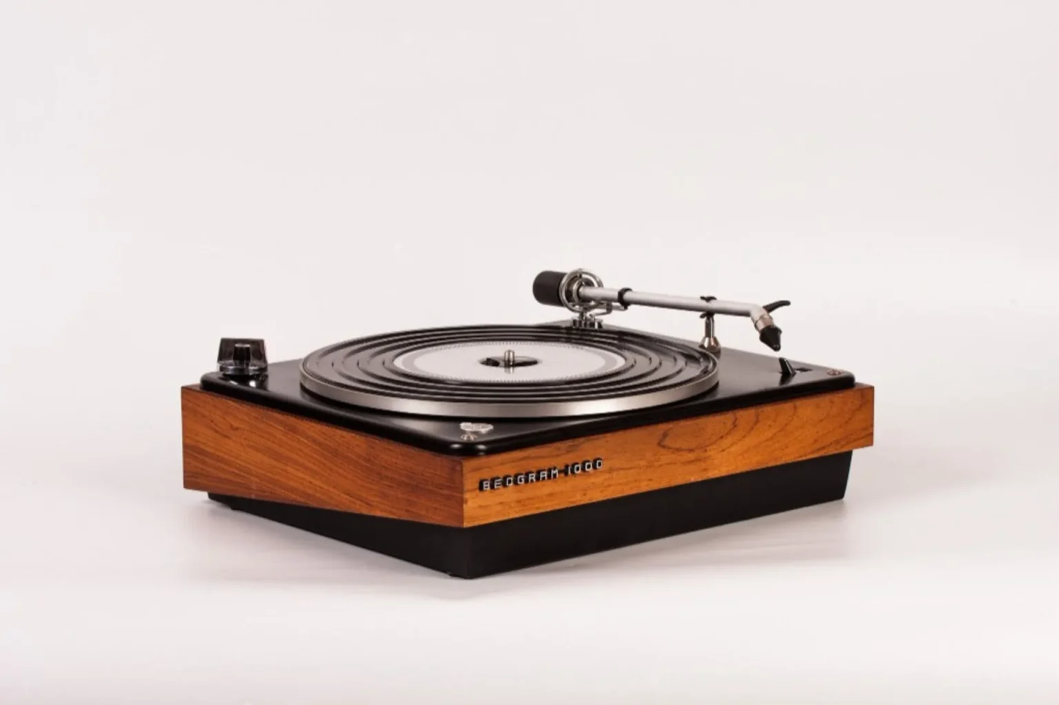 Close-up of Beogram 1000 silver tonearm over platter with black rubber mat and wood base, shallow depth of field.