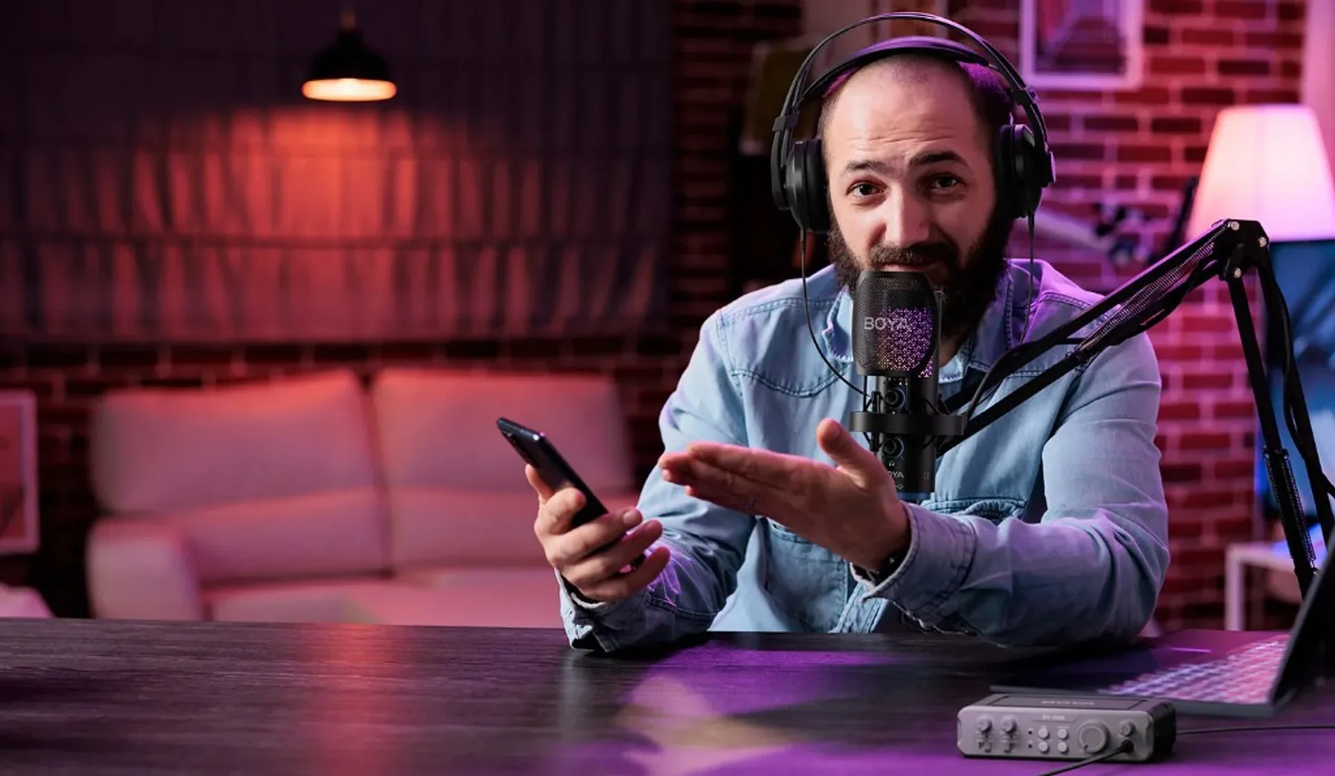 Creator at a desk with a BOYA large microphone on a boom arm, over-ear headphones, and RGB-style ambient lighting.