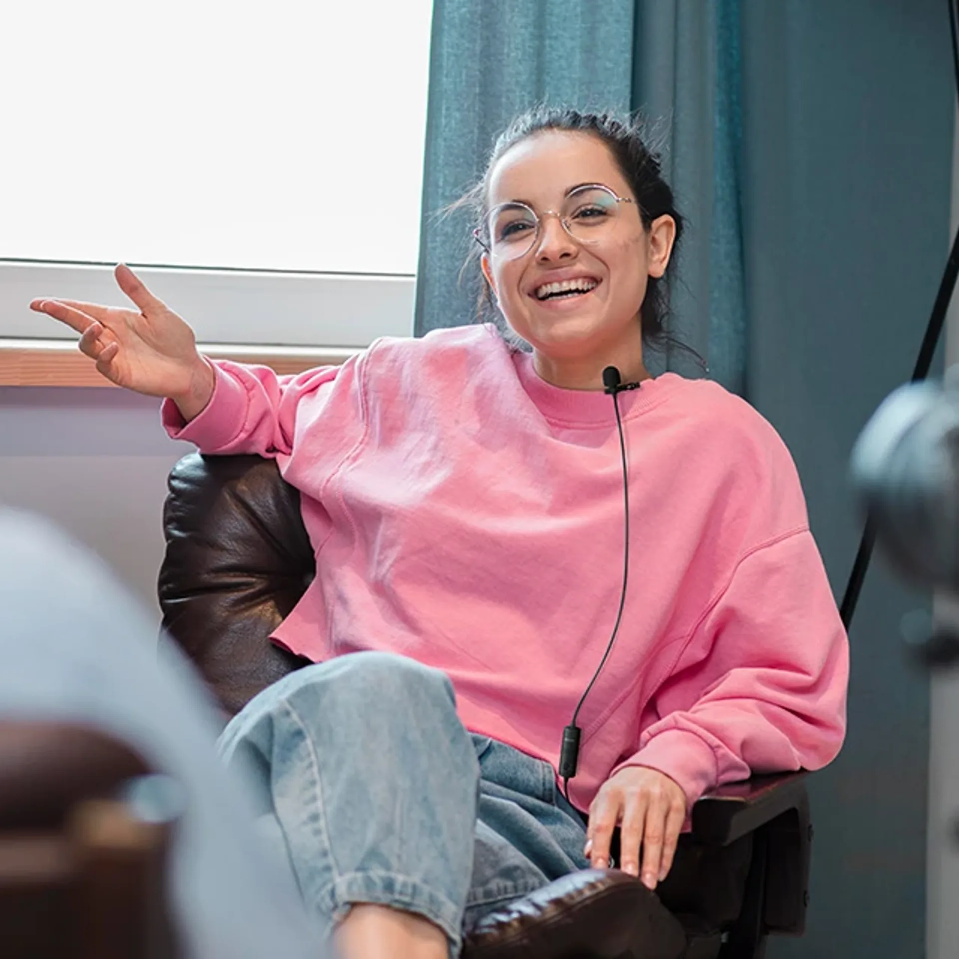 Woman in a chair with a BOYA wired lavalier microphone clipped to her collar, interview setting.