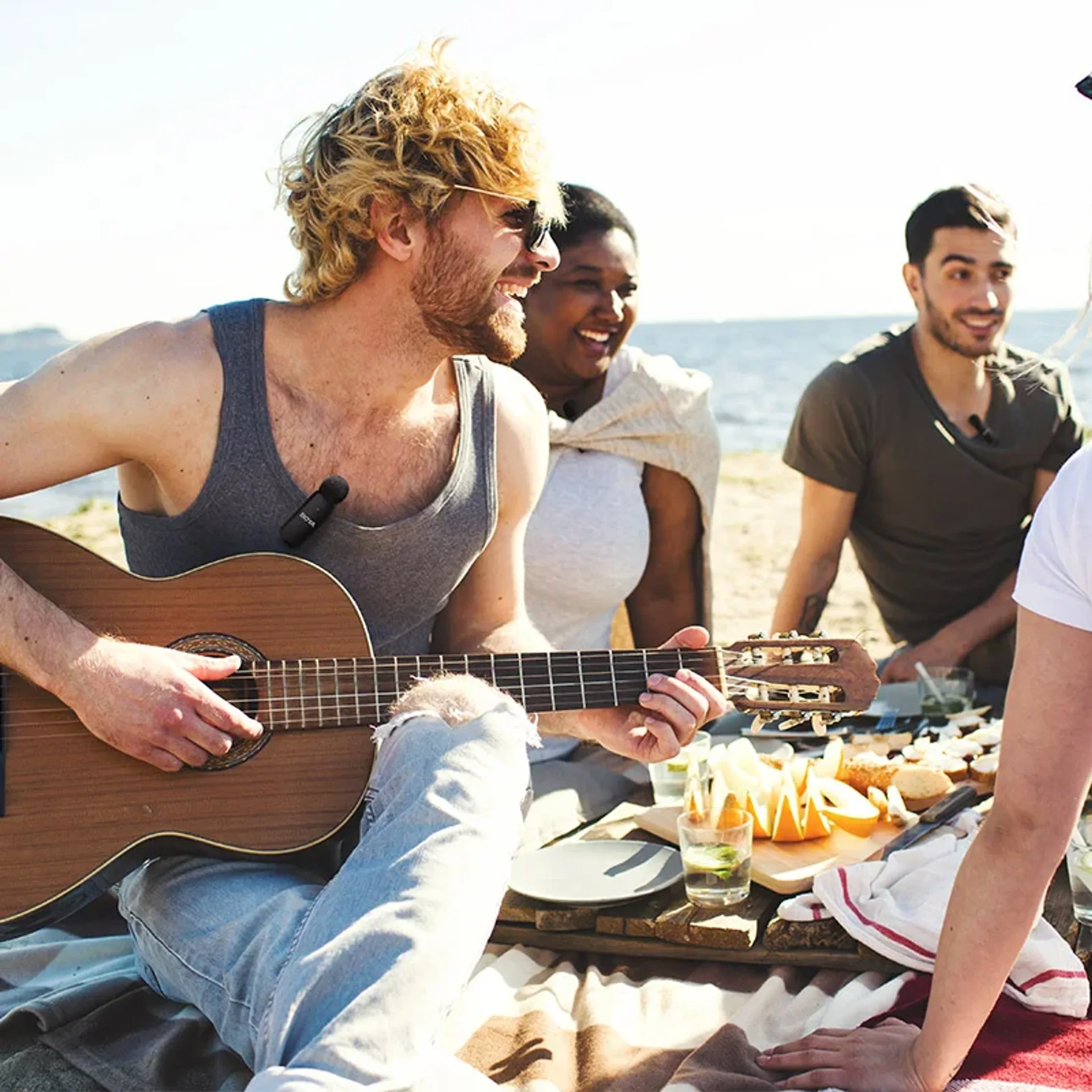 Beach picnic with a guitarist wearing a small BOYA wireless lapel microphone on his shirt.