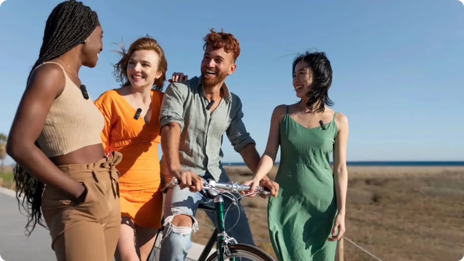 Four friends with BOYA wireless lapel mics outdoors near the coast, candid group shot.