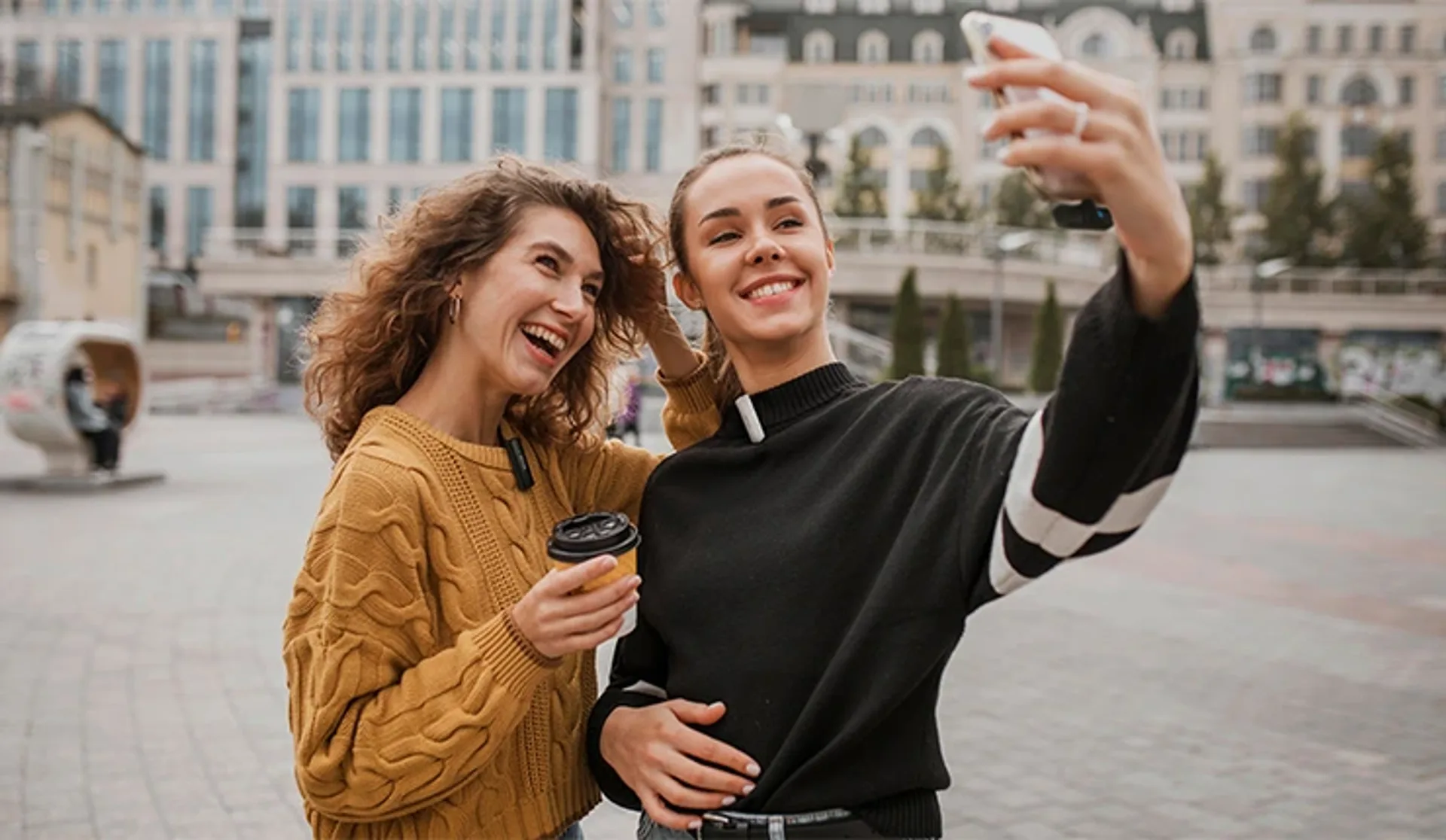 Two content creators in a city square with BOYA wireless mics and a phone on a selfie frame.