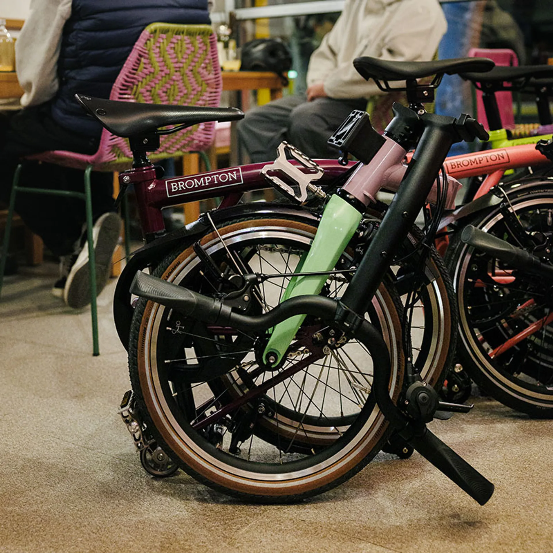 Brompton P Line Asia-Exclusive fully folded indoors: plum frame with Brompton logo, pink stem, mint fork, tan-wall tires and…