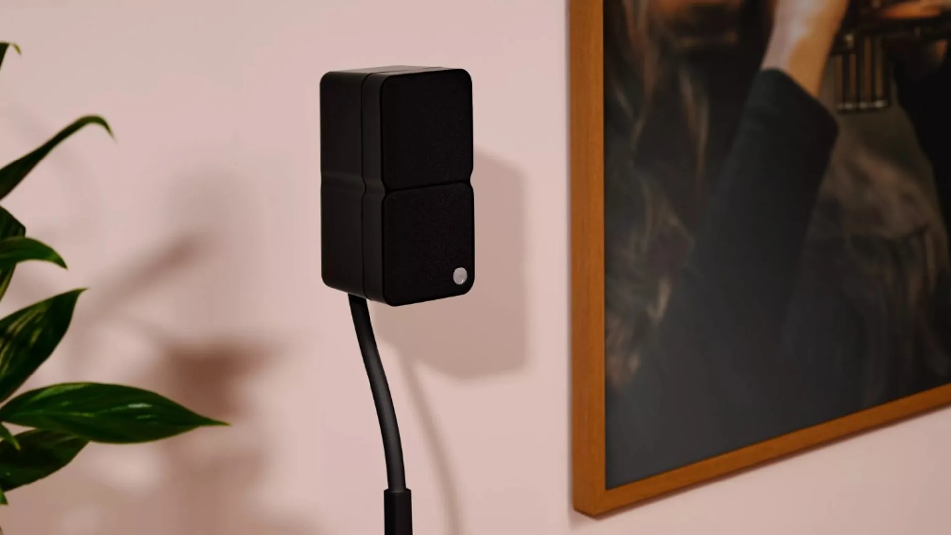 Black Cambridge Audio Minx tall satellite speaker with dual grilles on a slim floor stand, pale wall, houseplant and framed…