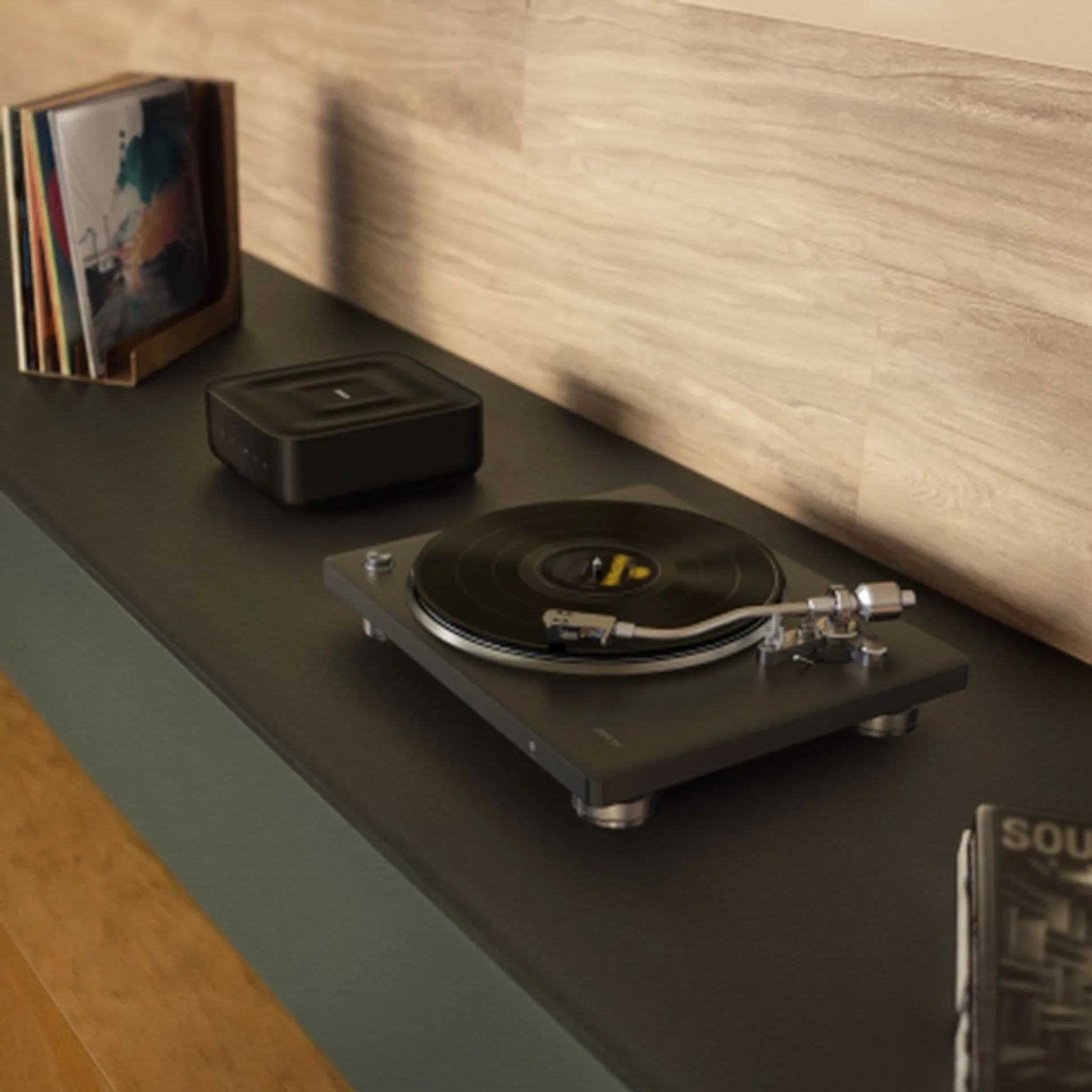 Denon DP-500BT on a dark shelf with Denon square speaker, vinyl rack and wood-paneled wall, warm natural light.
