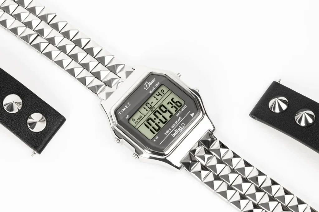 Dime x Timex T80 digital watch on white: silver studded bracelet, LCD with Timex and Dime logos, spare black leather strap s…