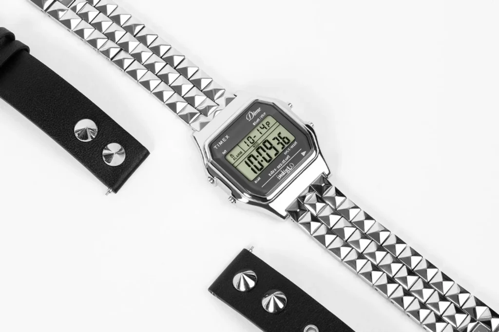 Dime x Timex T80 silver digital watch with pyramid stud bracelet and Indiglo bezel text, diagonal layout with black leather…
