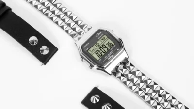 Dime x Timex T80 silver digital watch with pyramid stud bracelet and Indiglo bezel text, diagonal layout with black leather…
