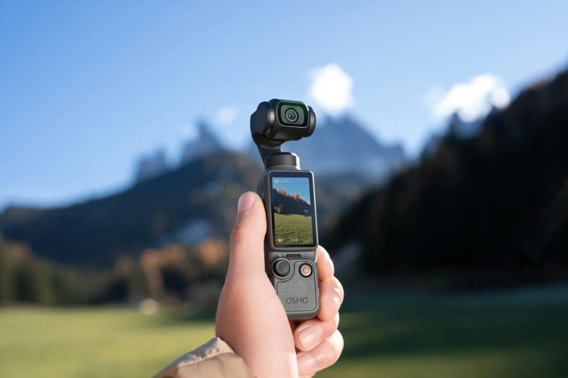 Hand holding a DJI Osmo Pocket gimbal camera with live preview against mountain scenery.