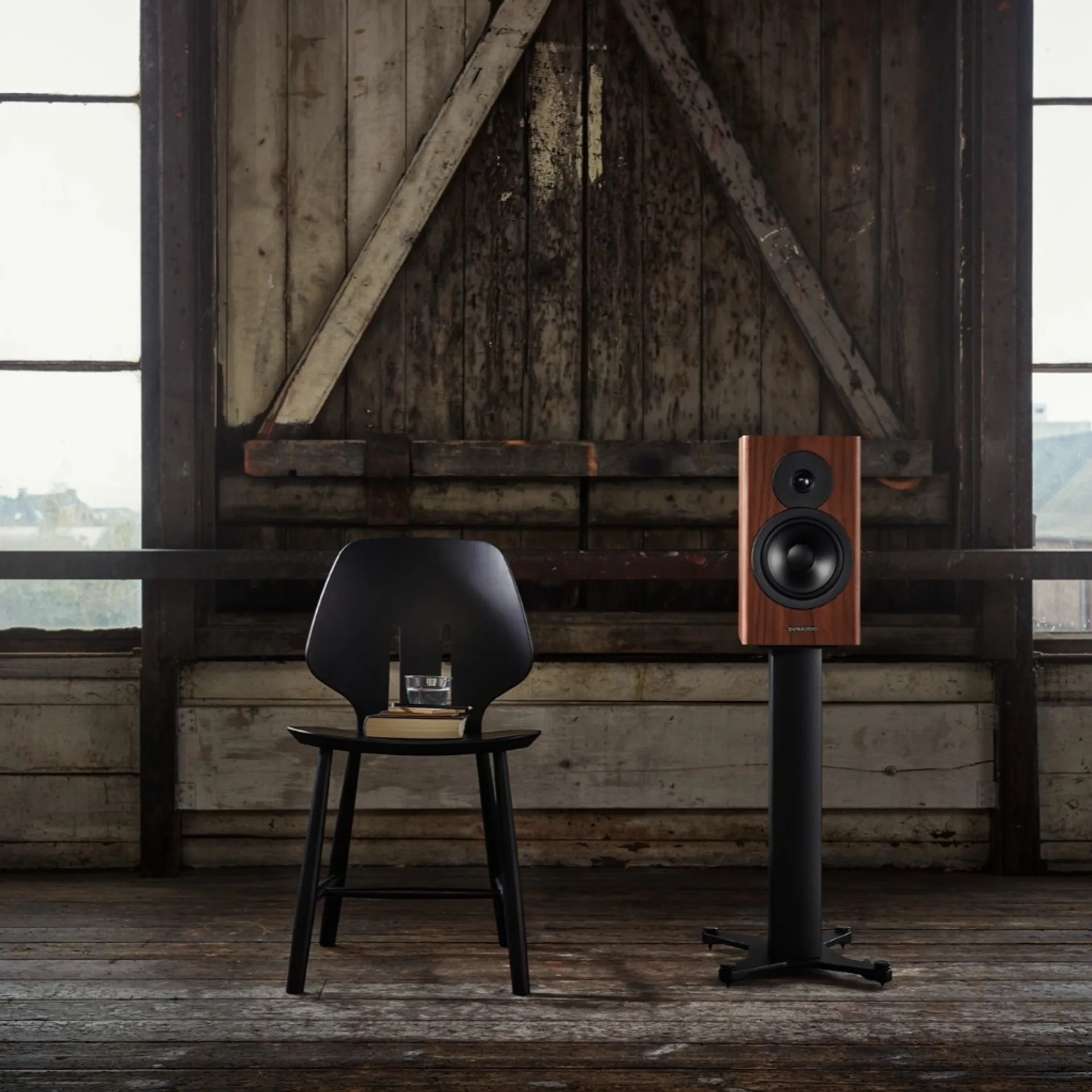 Dynaudio Evoke 20 veneer gỗ óc chó trên chân loa đen, phòng rustic sàn gỗ và cửa barn