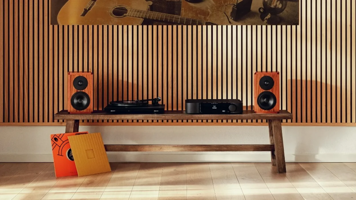 Pair of Dynaudio Heritage Special walnut bookshelf speakers flanking a turntable and MOON integrated amplifier on a rustic b…