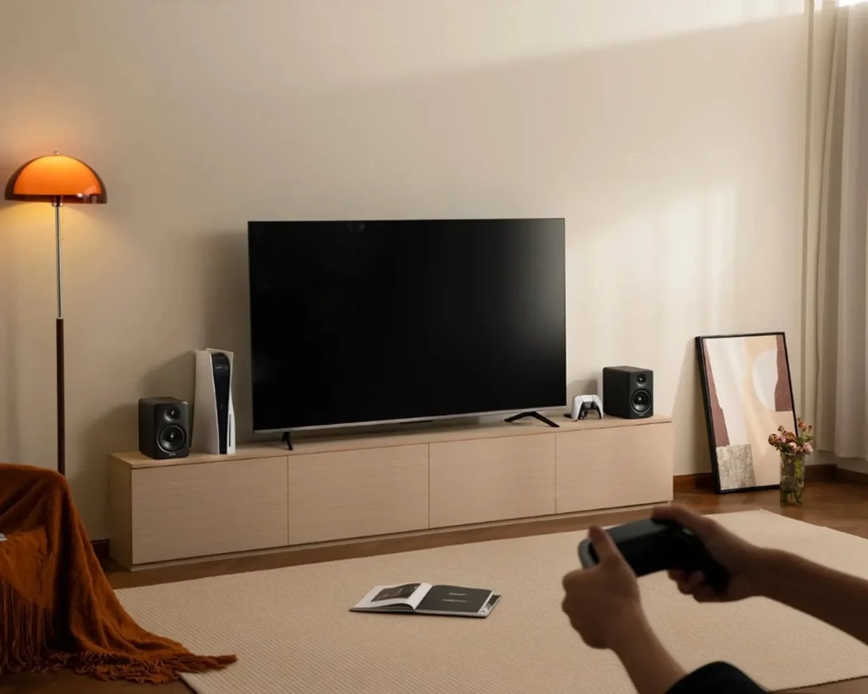 Edifier M90 black bookshelf speakers flanking a TV on a light wood console with PlayStation 5 and gaming controller.