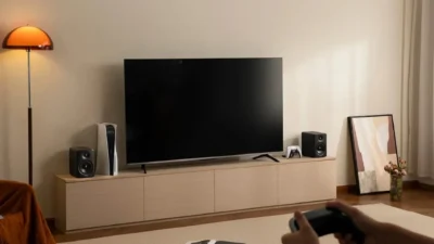 Edifier M90 black bookshelf speakers flanking a TV on a light wood console with PlayStation 5 and gaming controller.