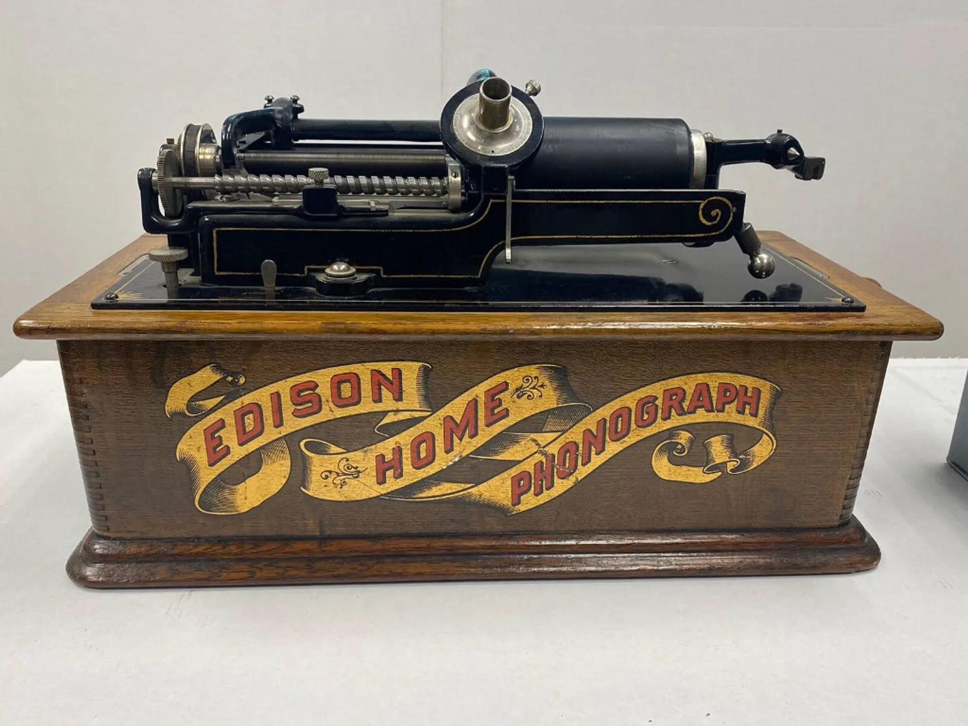 Antique Edison Home Phonograph with oak cabinet, yellow scroll label, and black metal cylinder playback mechanism.