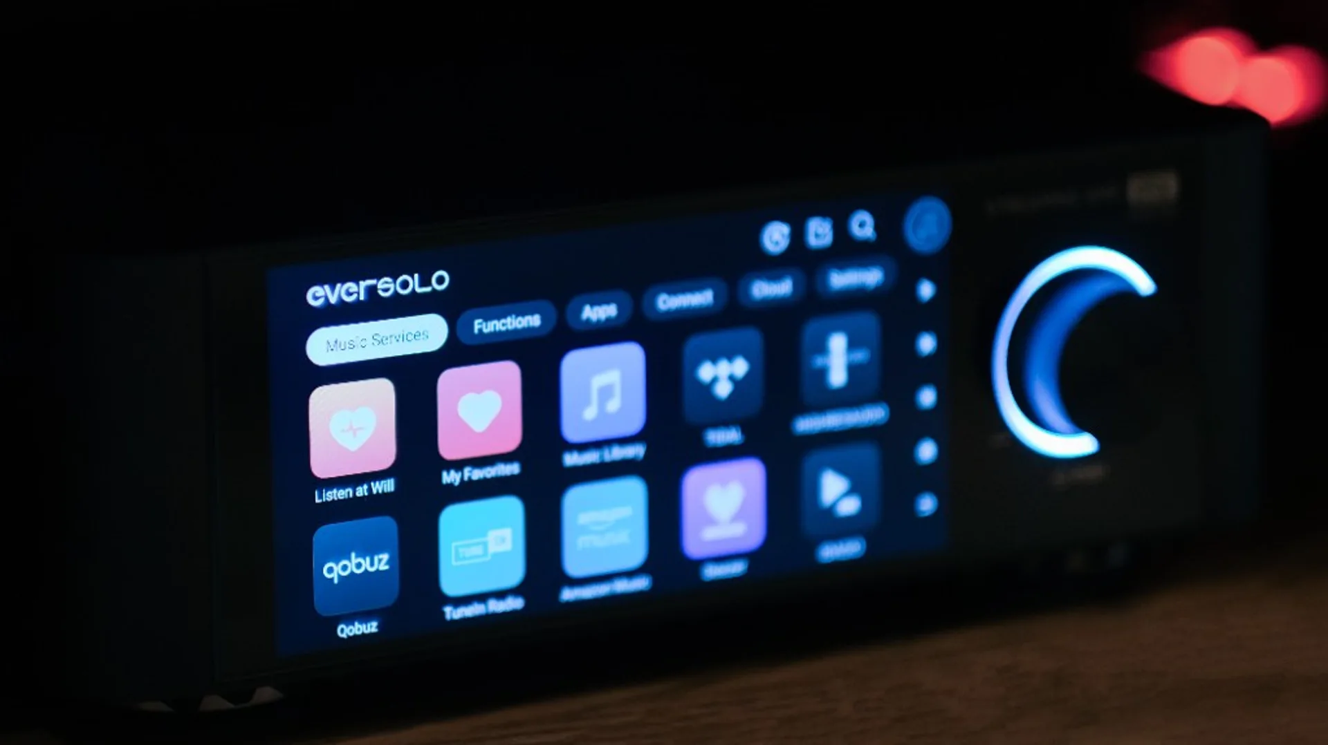 Close-up of an Eversolo audio streamer touchscreen showing Music Services with Tidal, Qobuz, Amazon Music and a blue-lit vol…
