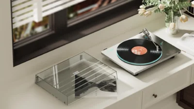 FiiO TT13 automatic turntable placed on a white console in a living room, top perspective with dust cover beside it.