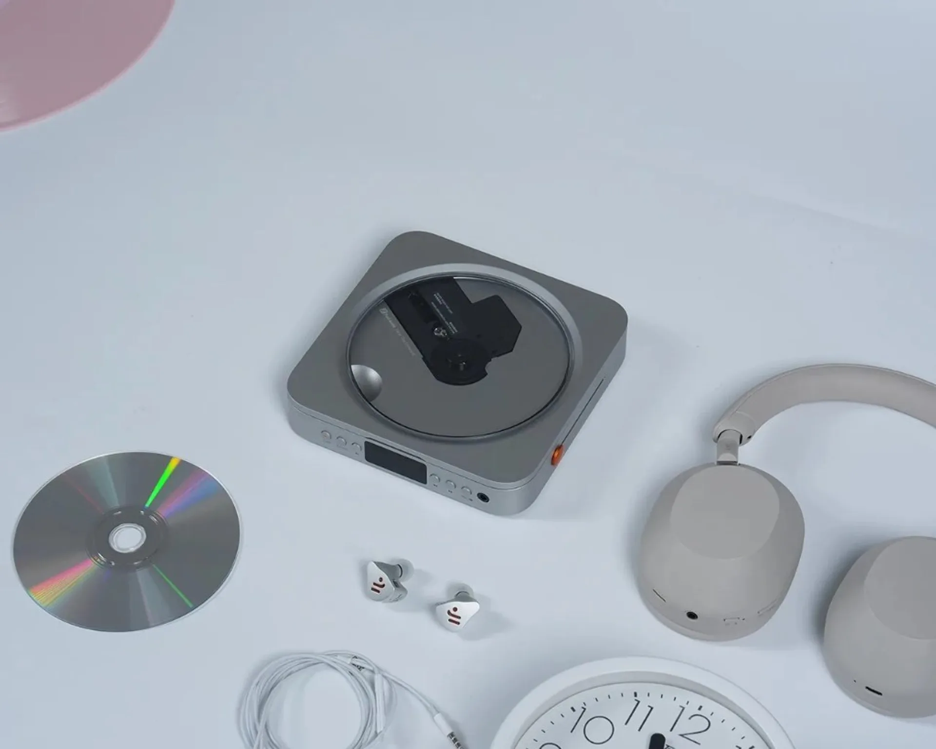 Top-down product shot: Fosi Audio Merak CD player with visible disc mechanism, loose CD, grey headphones, white IEMs and cab…