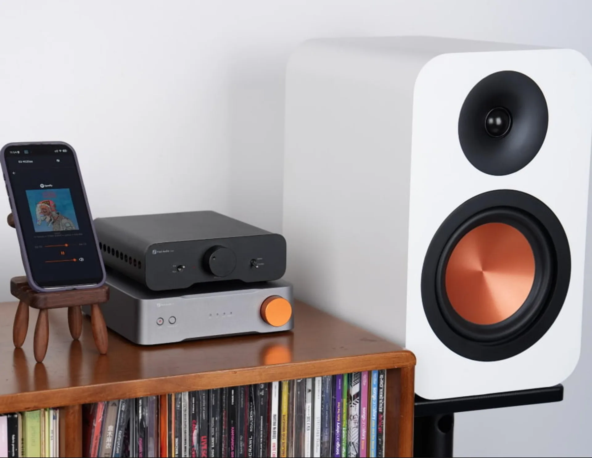 Fosi Audio S3 xếp chồng ampli Fosi trên kệ gỗ, điện thoại Spotify và loa bookshelf đồng woofer