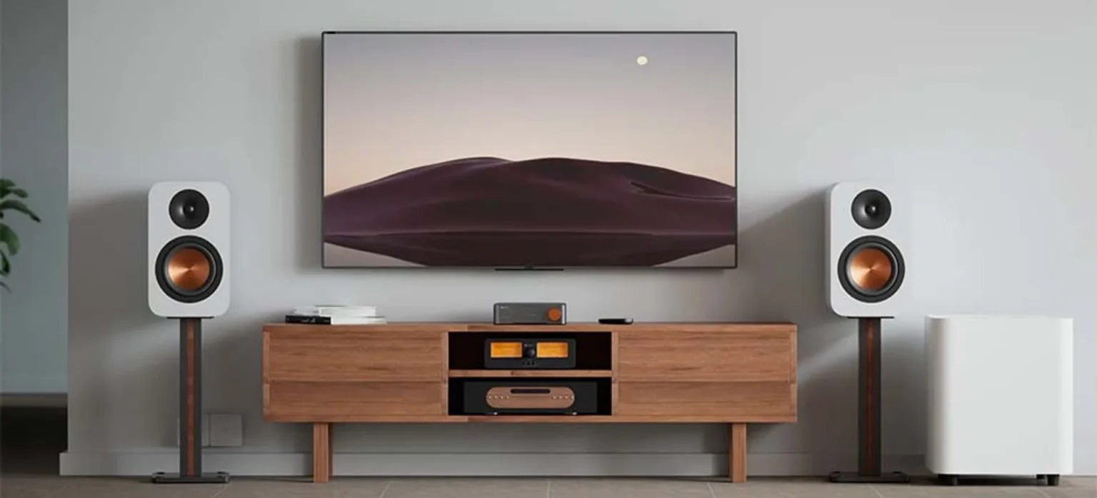 Phòng khách với TV treo tường, kệ gỗ và Fosi Audio S3 cùng loa bookshelf trắng trên chân
