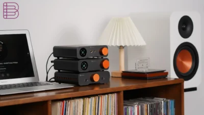 Three stacked Fosi Audio black components with displays and copper knobs on a dark wood console beside a laptop and white bo…