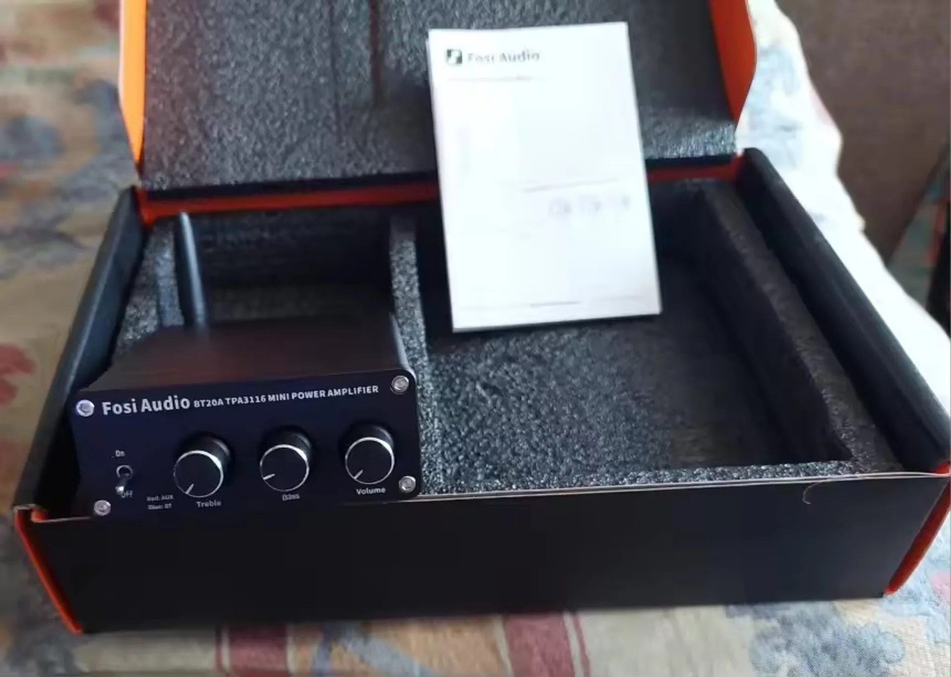 Fosi Audio BT20A amplifier placed in the box during unboxing with manual in the background.