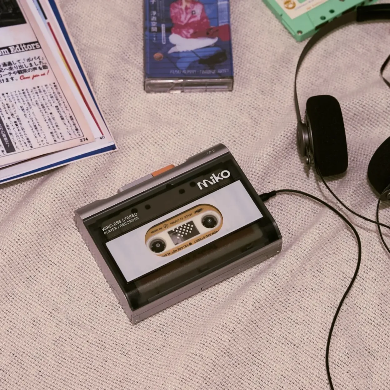 Gadhouse Miko wireless stereo cassette player on textured fabric with headphones, cassette cases, mint accent and magazine,…