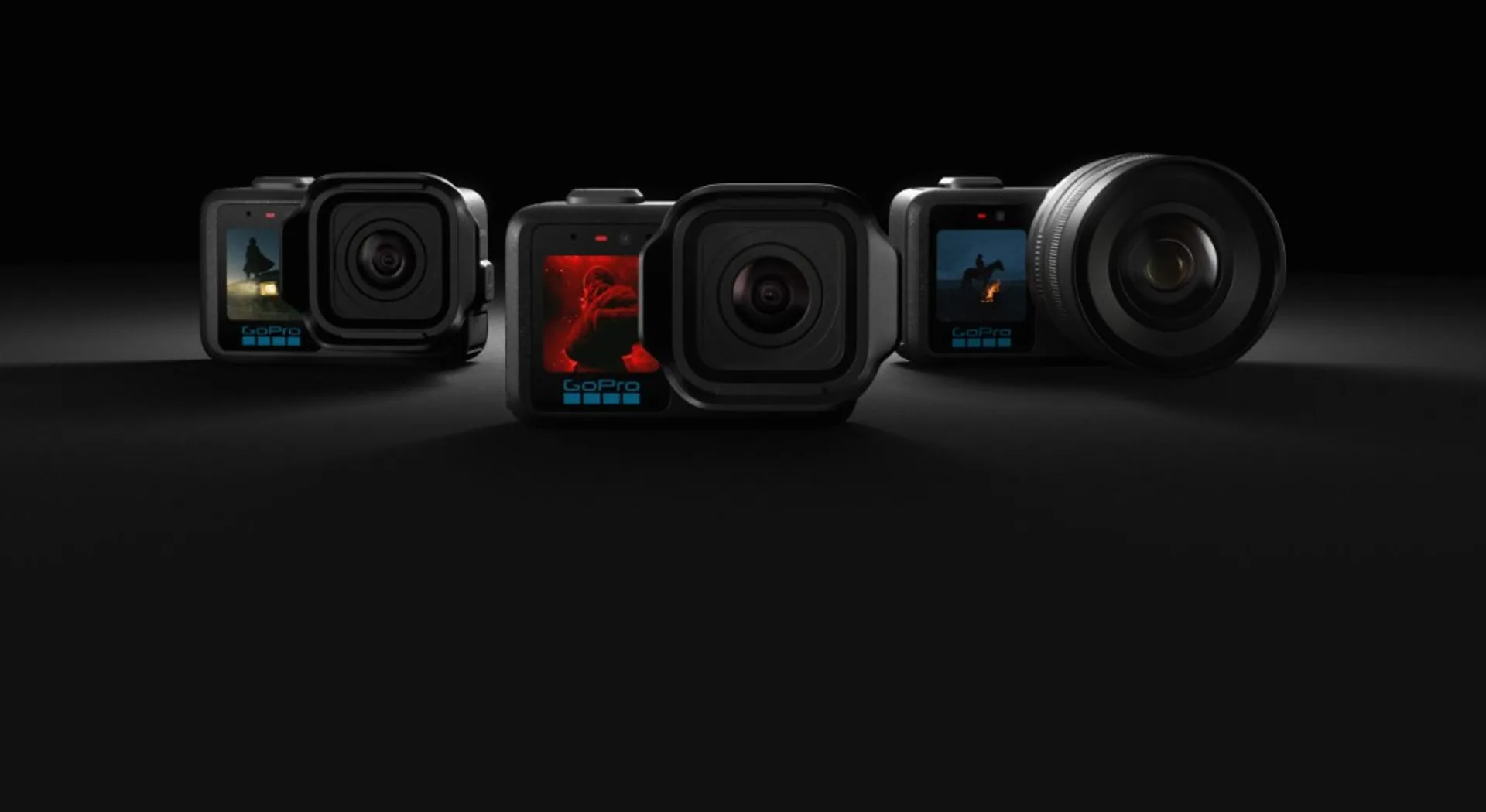 Three GoPro Mission 1 style cameras on black reflective surface showing modular lens options: compact module and large prime…