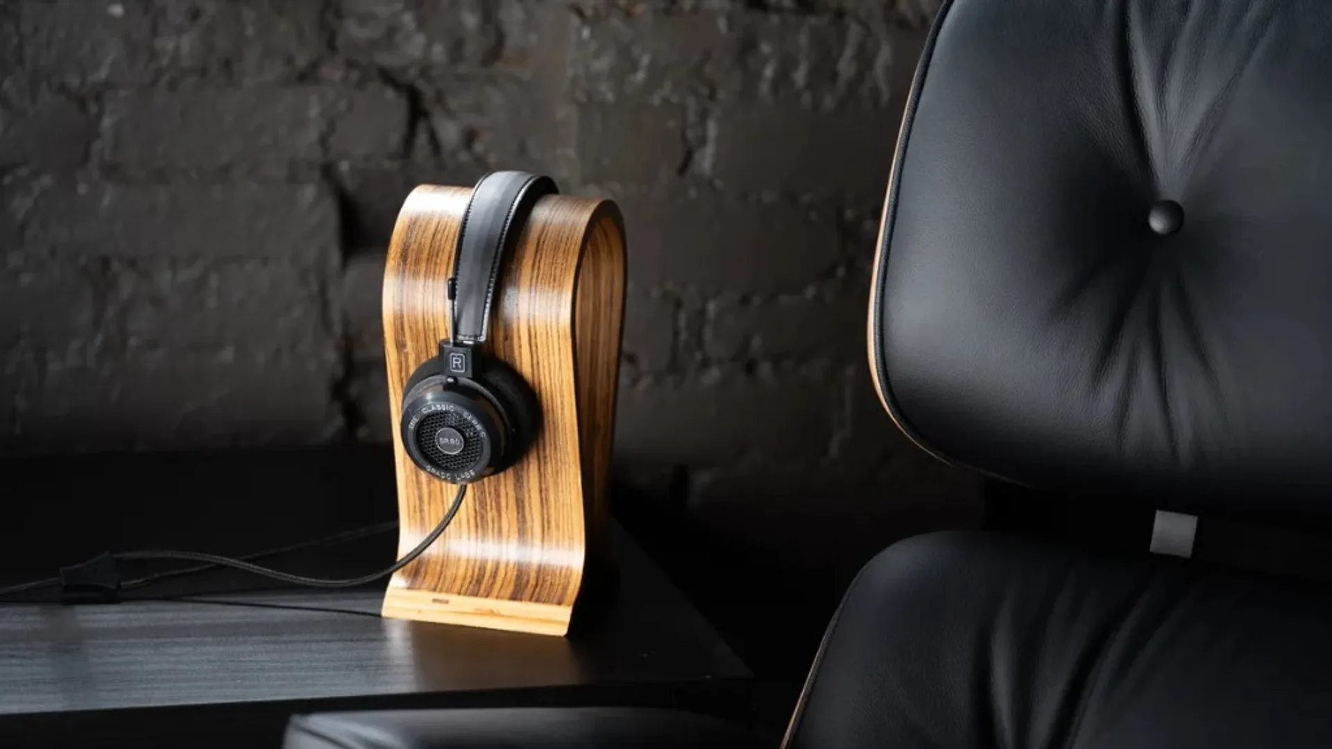 Grado SR60 open-back Classic Series headphones on a curved wooden stand against a dark brick wall with a black leather loung…