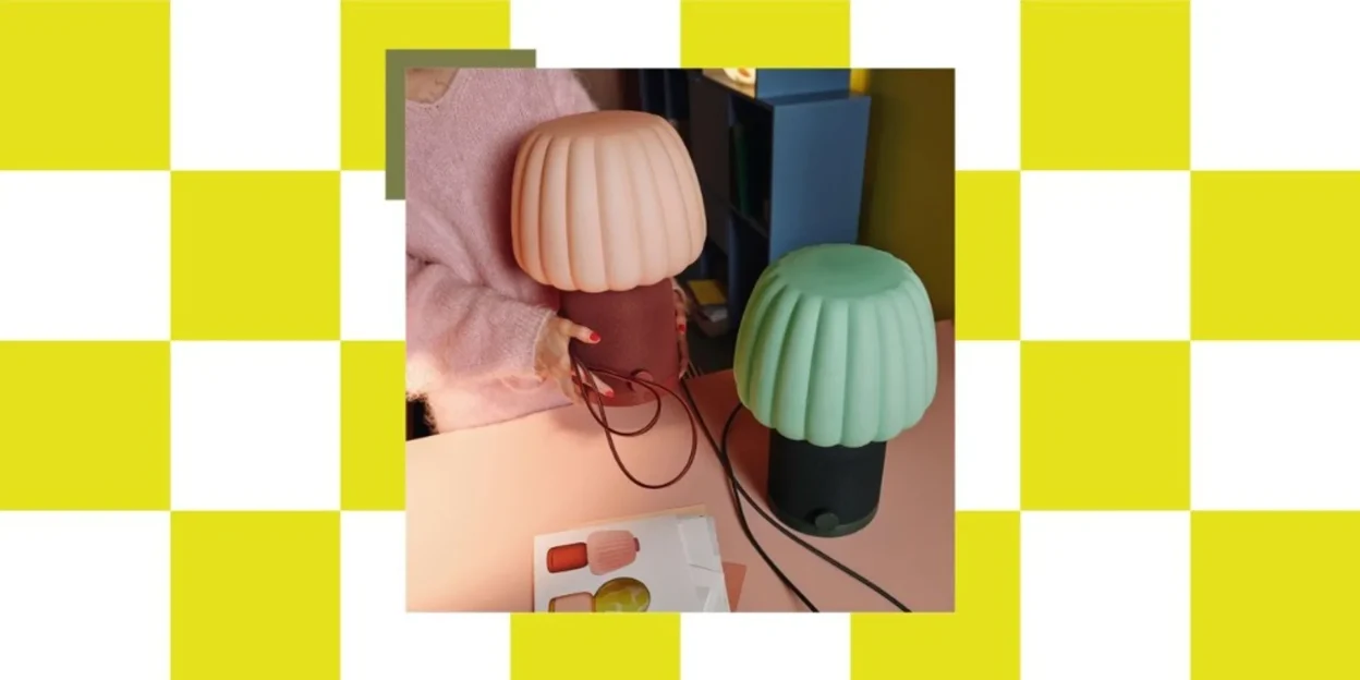 Lifestyle scene with peach and mint green IKEA KULGLASS mushroom speaker lamps on a pink table, checkerboard frame, hands ho…