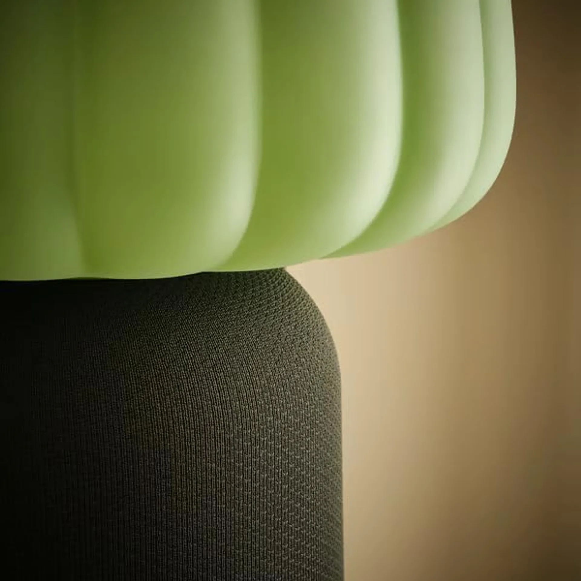 Close-up of IKEA KULGLASS lamp: light green ribbed frosted glass shade meeting a dark green knitted fabric speaker base.