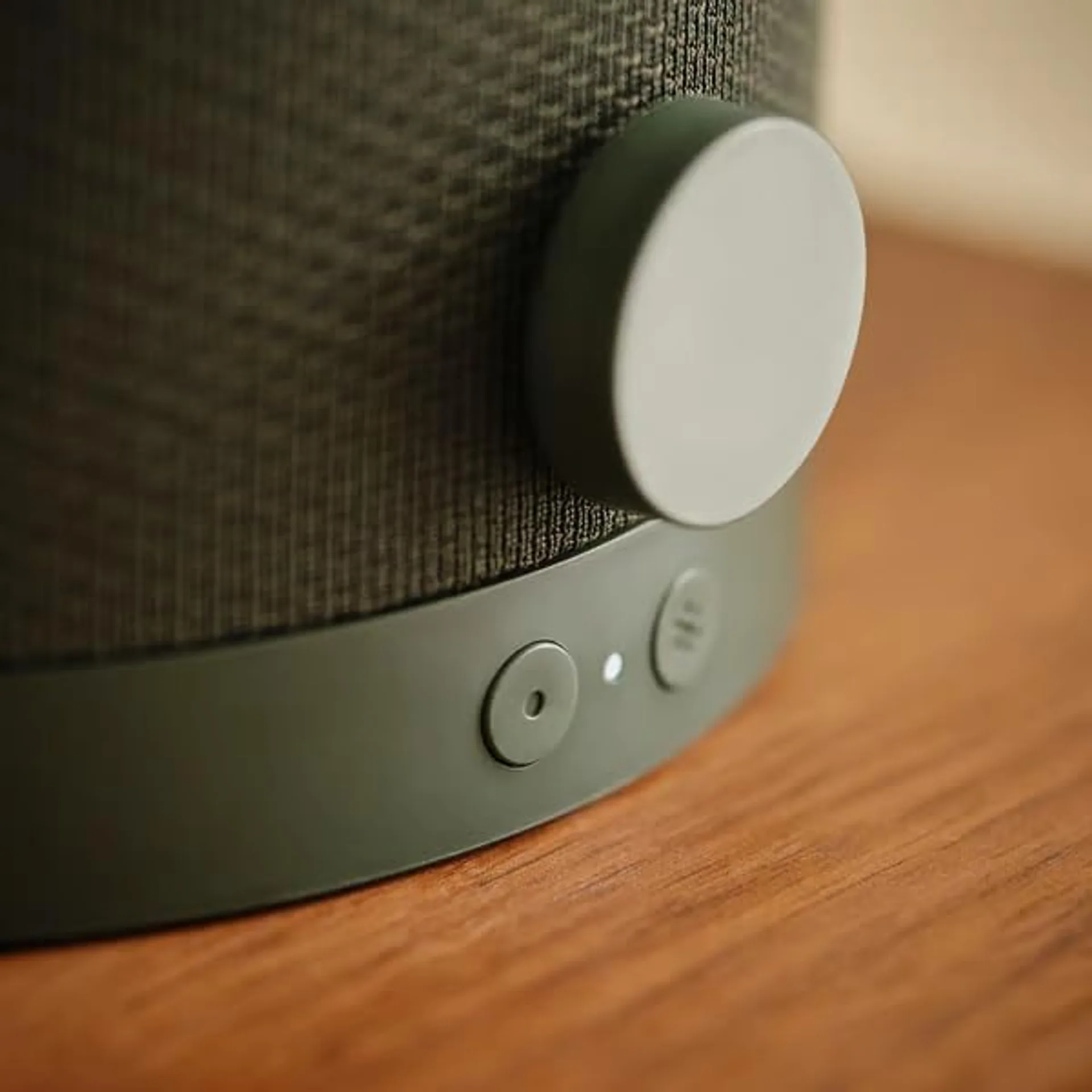 Close-up of olive green IKEA KULGLASS speaker lamp controls: mesh fabric, circular volume dial, and playback buttons on wood.