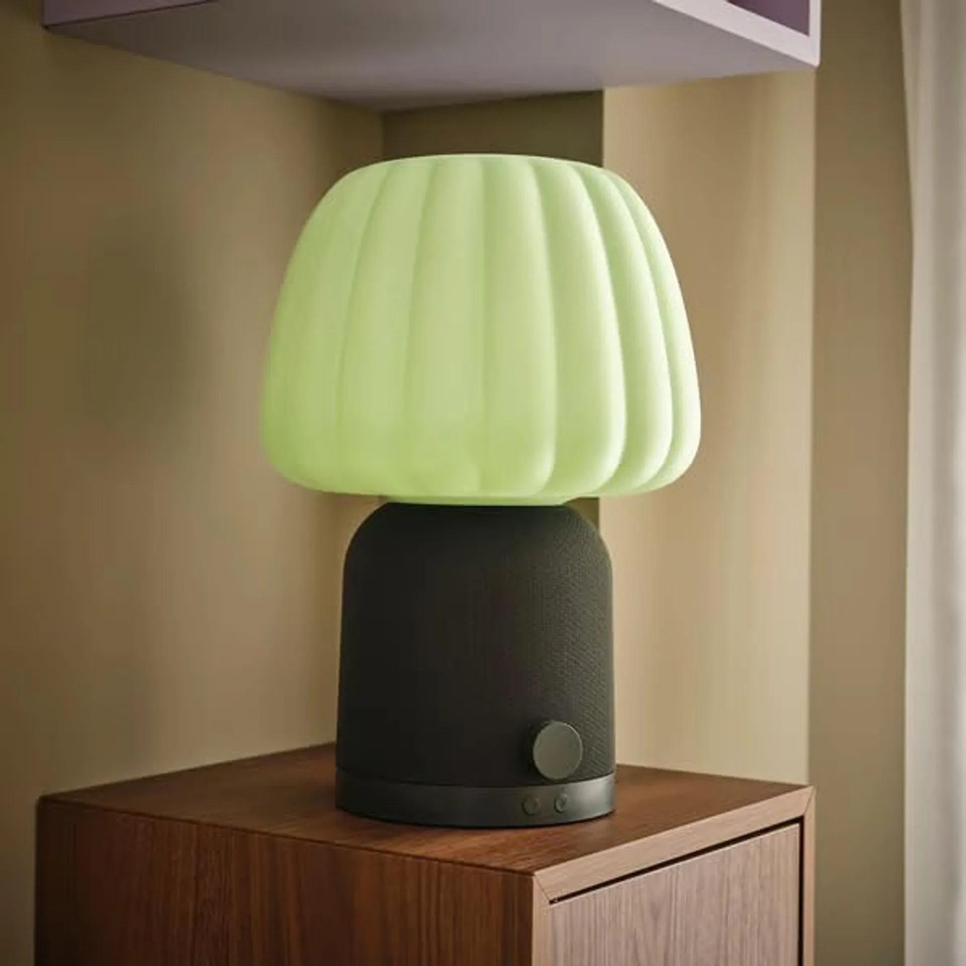 IKEA KULGLASS SYMFONISK speaker lamp with pale green fluted glass shade and black fabric Sonos base on a walnut cabinet in a…