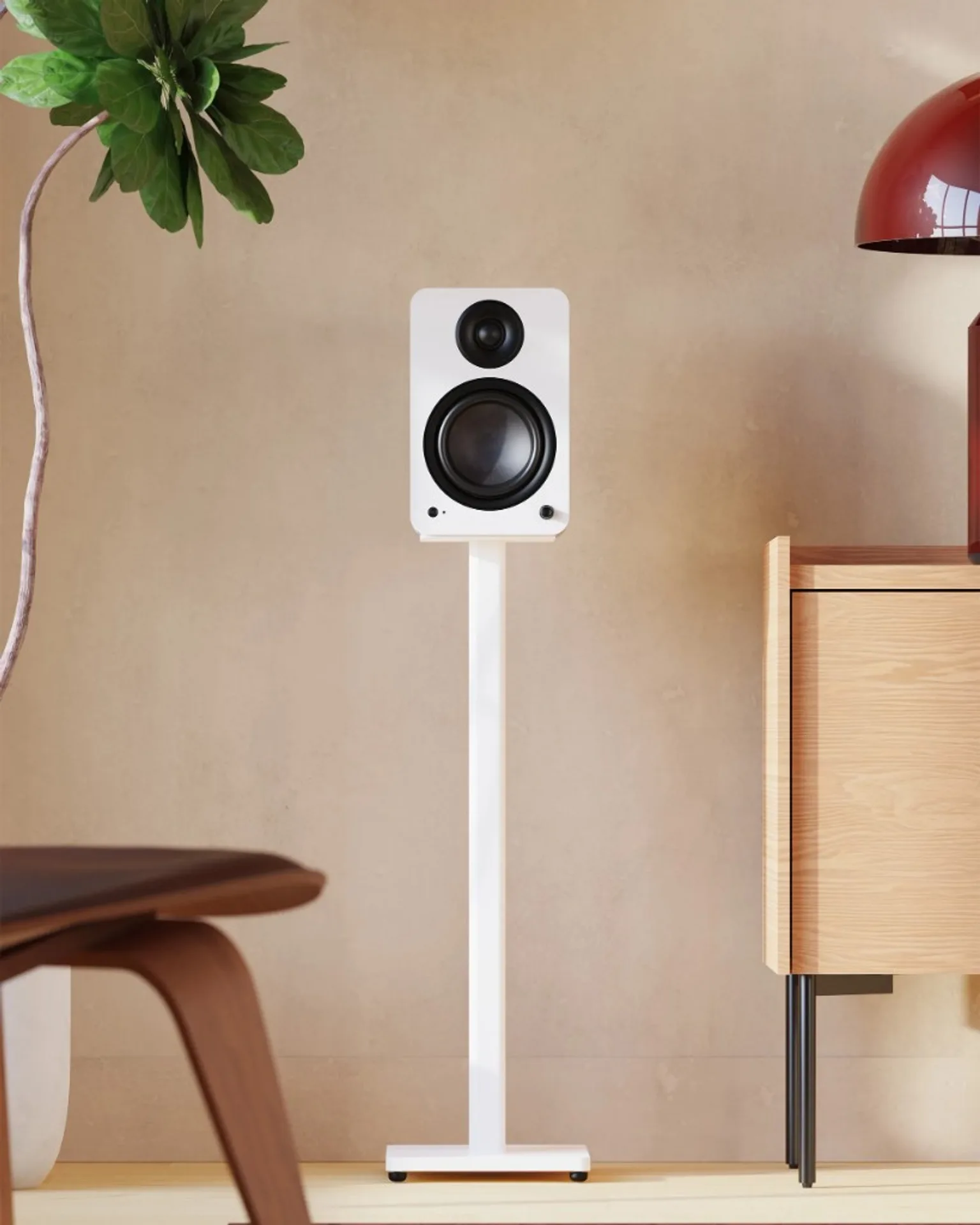 Matte white Kanto bookshelf speaker on tall white floor stand in a neutral modern room with wood sideboard and plant.