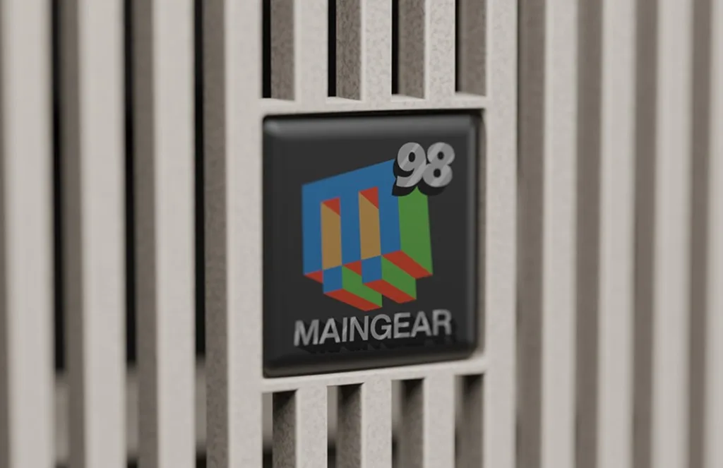 Close-up of Maingear 98 logo badge with colorful 3D block M on a light slatted computer case panel.