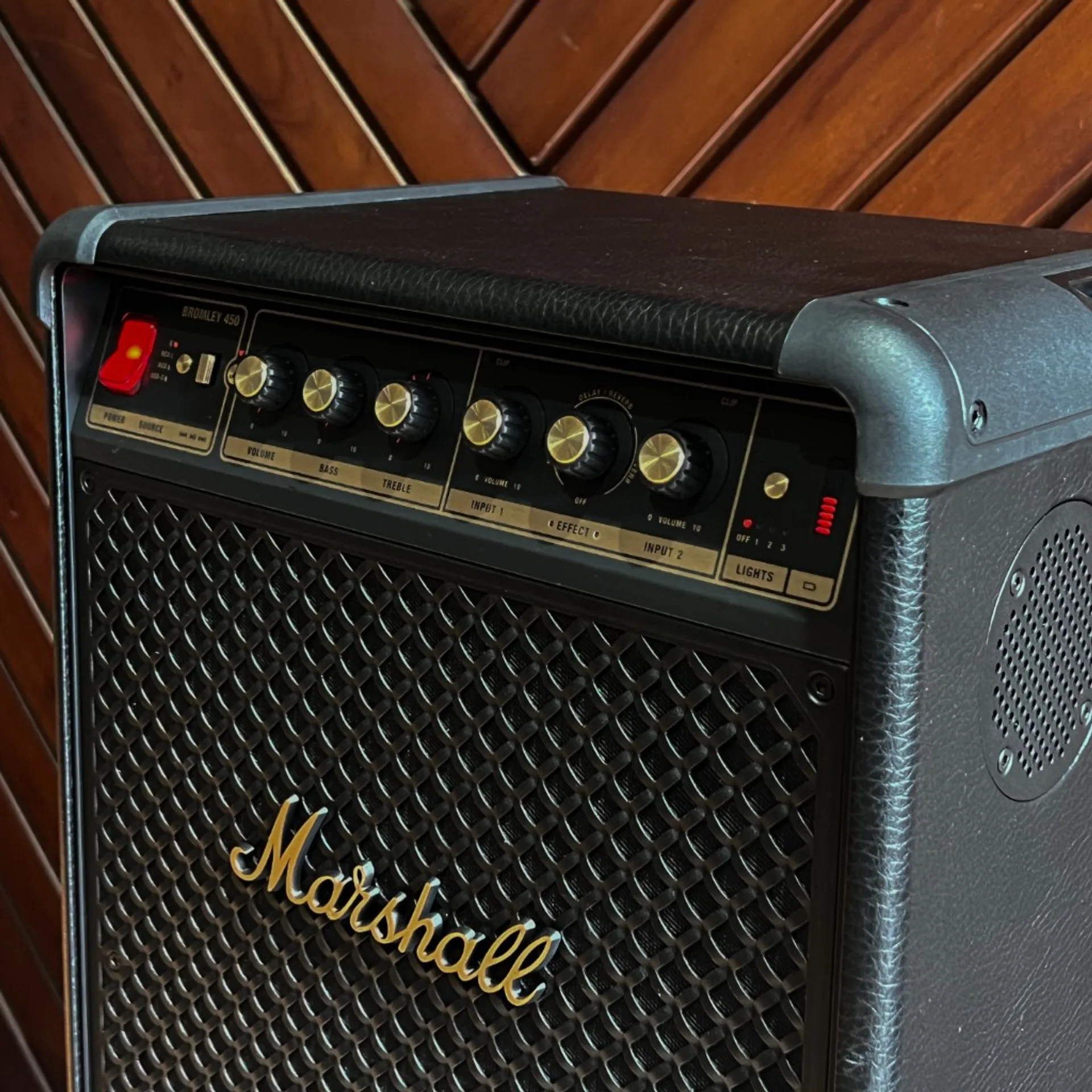 Marshall Bromley 450 at an angle: black tolex, corner caps, woven grille with gold Marshall logo, top panel with Volume Bass Treble mic and effect knobs against wood panels.
