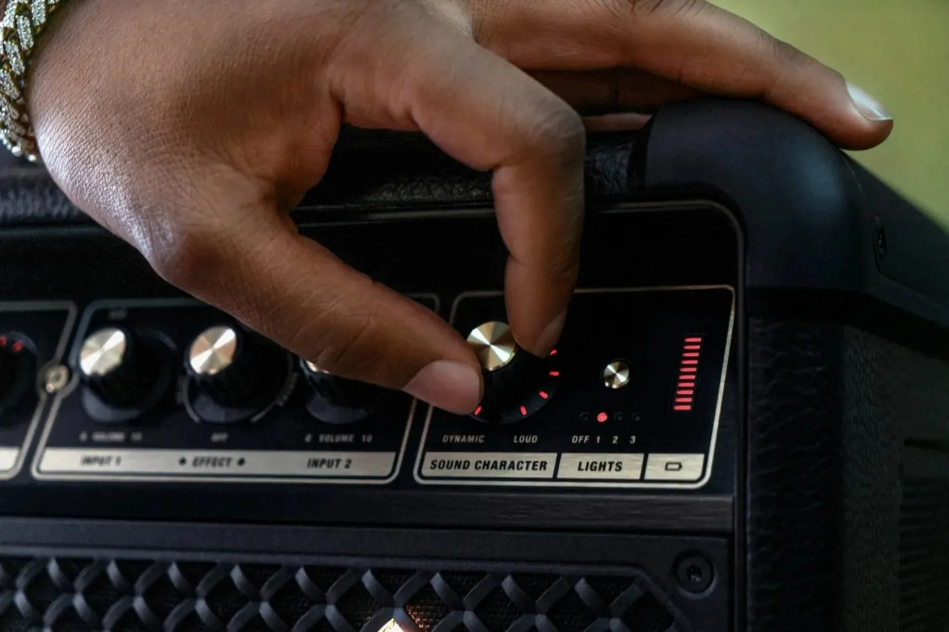 Marshall portable speaker on wet asphalt with gold logo and extended handle beside a classic black car with chrome wheels, u…