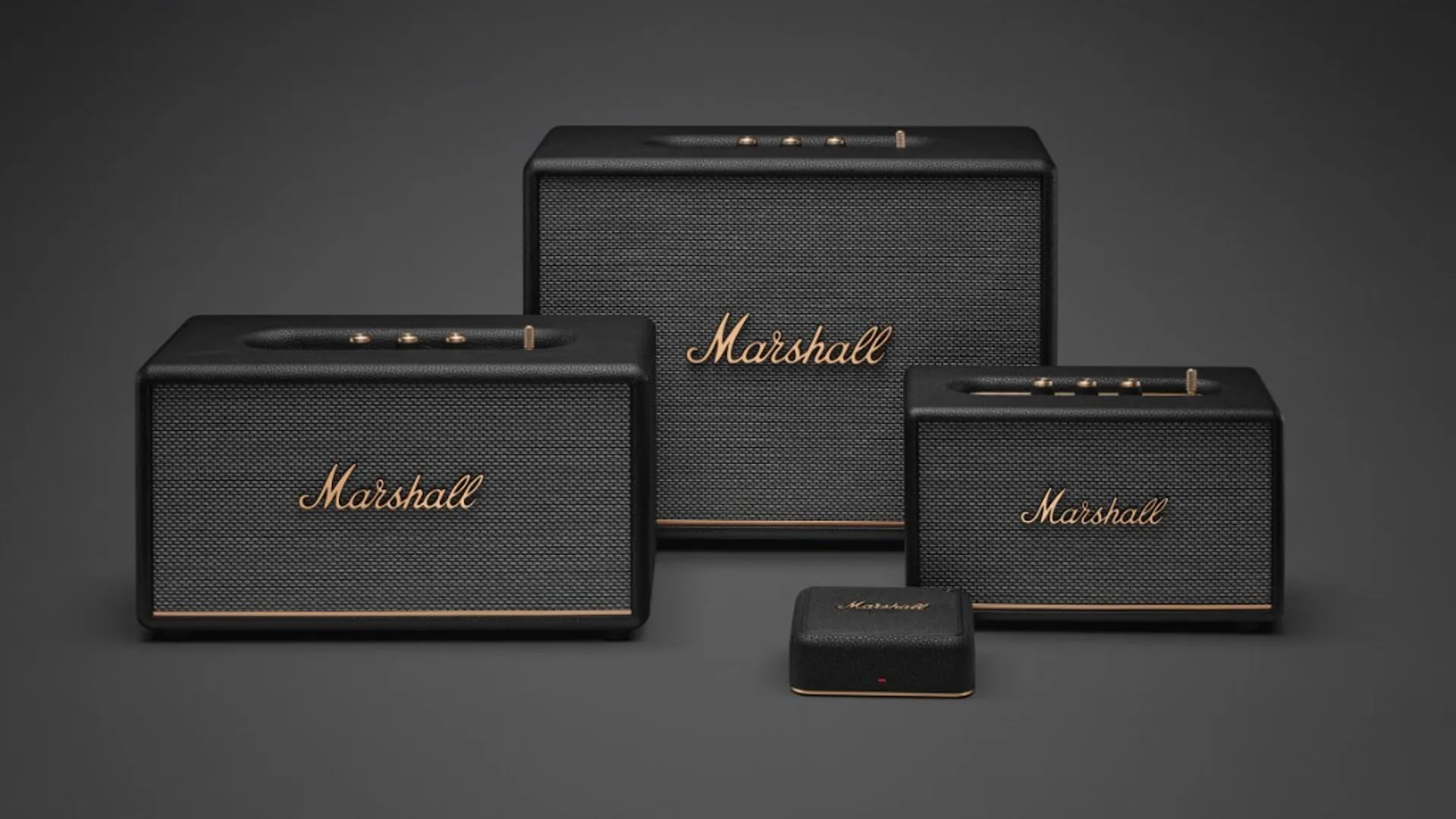 Studio lineup of three black Marshall speakers plus small square Marshall unit, brass logos and control strips, dark grey ba…