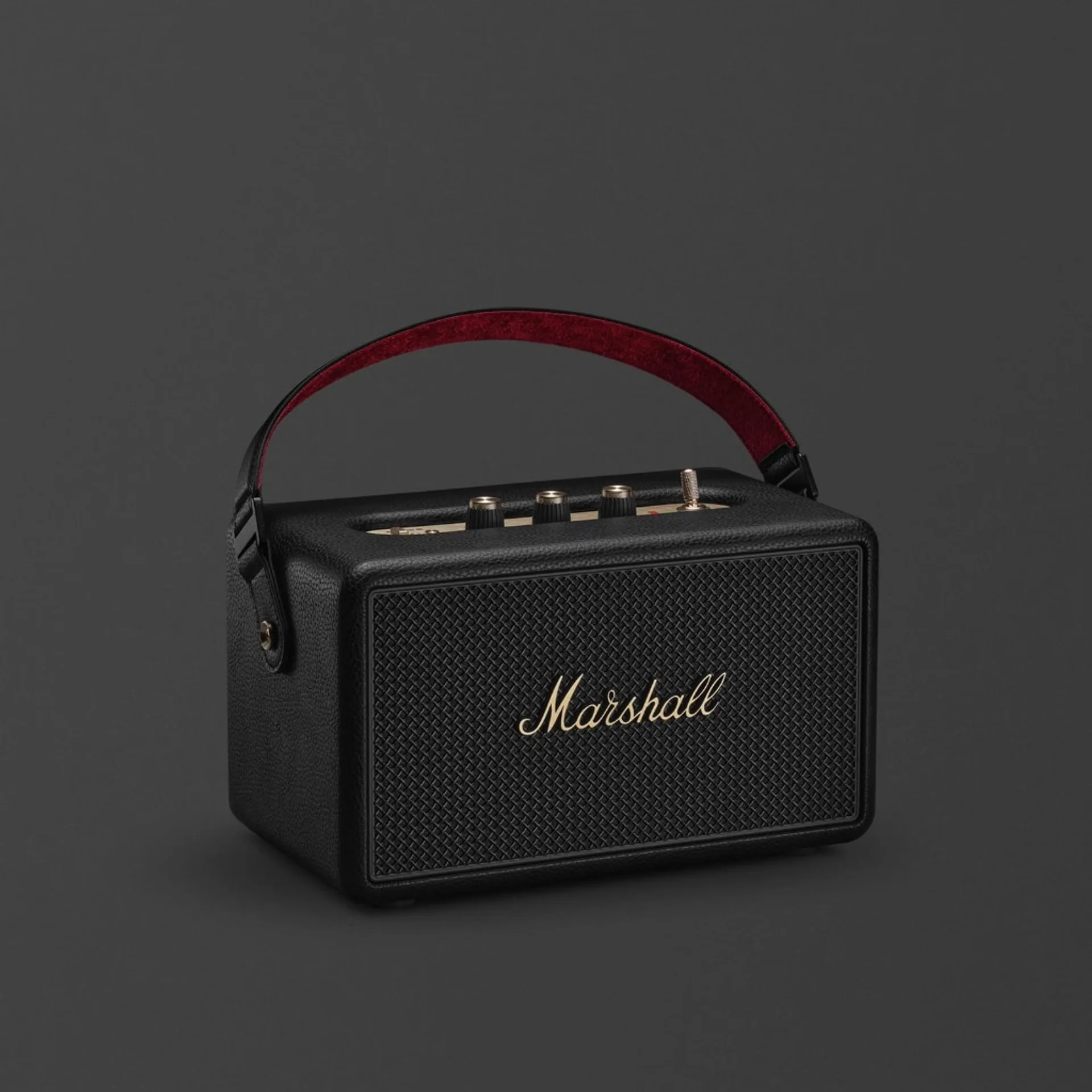 Marshall Kilburn III portable speaker three-quarter on charcoal grey: black tolex, gold script logo on grille, brass top con…
