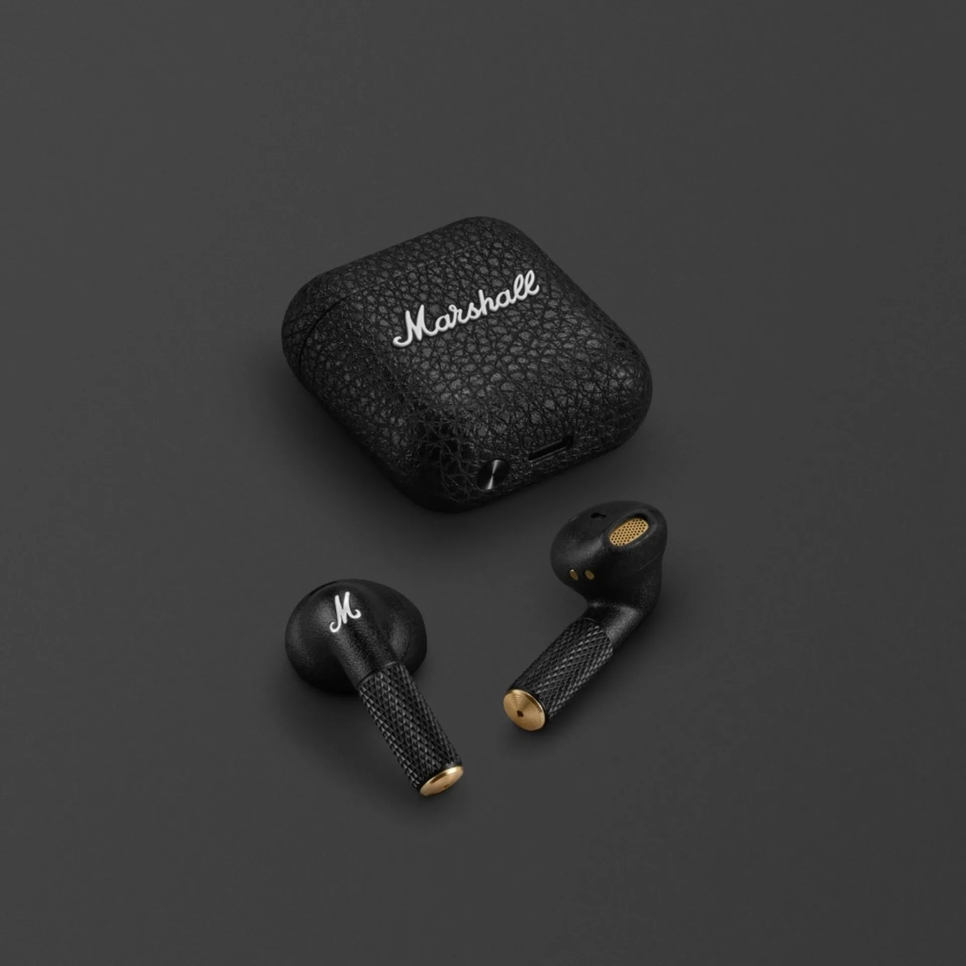 Marshall Minor IV true wireless earbuds and pebble-grain case with brass stem caps on dark grey studio background.