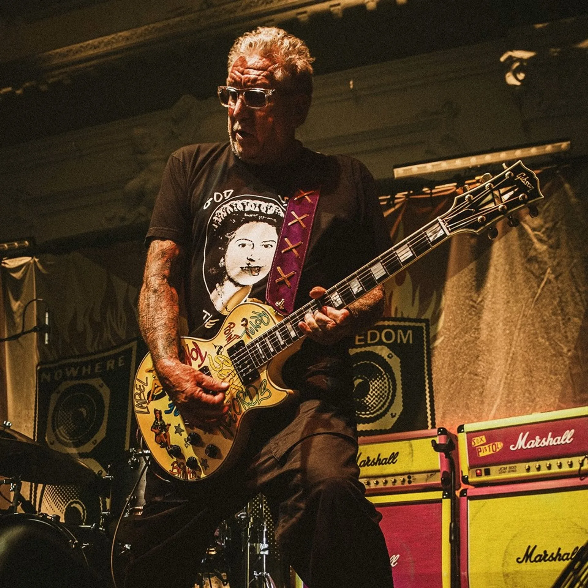 Steve Jones of Sex Pistols on stage with Gibson Les Paul and Marshall x Sex Pistols JCM800 stacks in pink and yellow under l…
