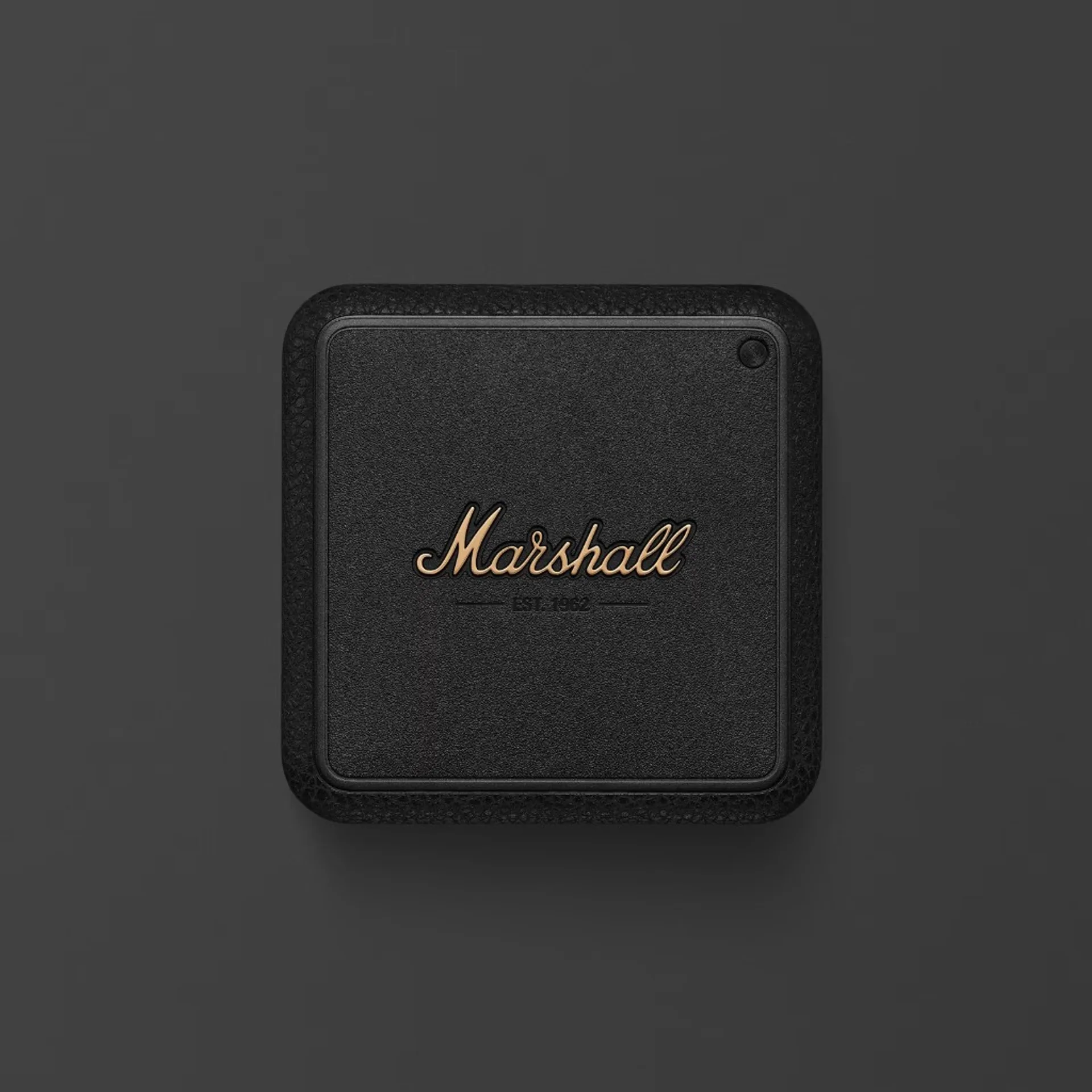 Top-down product shot of black Marshall Willen portable speaker with brass script logo and EST 1962 on dark charcoal backgro…