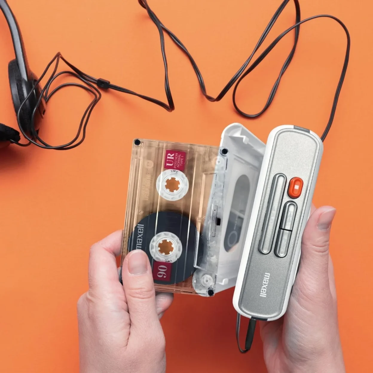 Top-down view of hands loading a Maxell UR 90 cassette into a white and silver Maxell portable cassette player on a bright o…