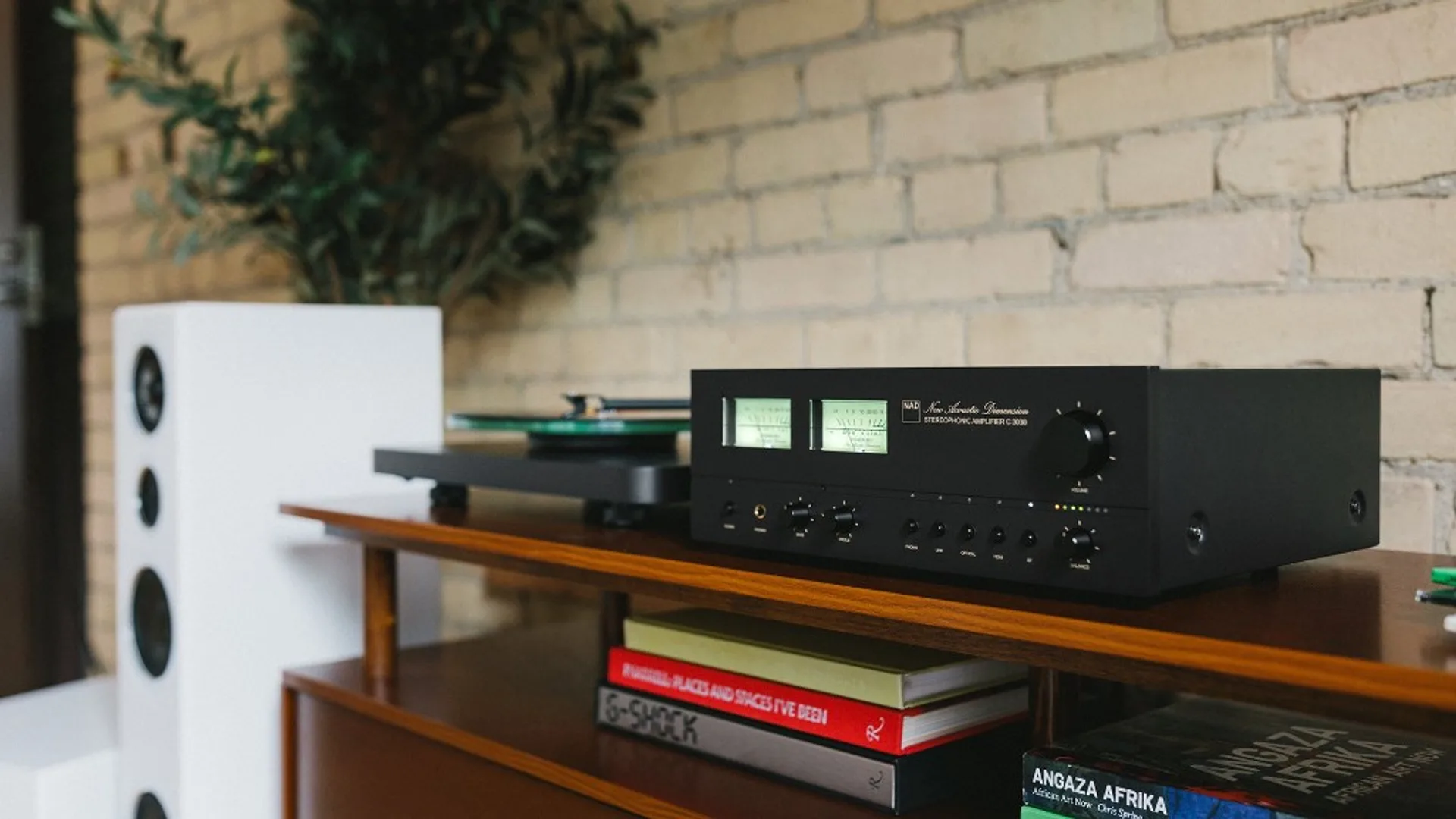 NAD C 3030 on a credenza beside a turntable and bookshelf speaker in a home listening setup.