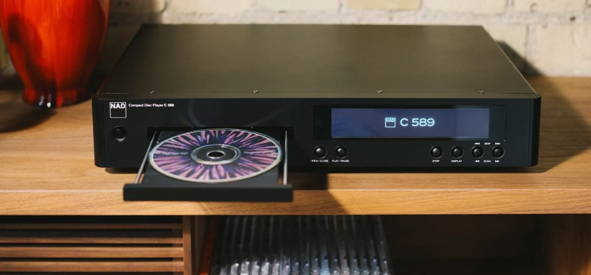 NAD C 589 on wood shelf with open disc tray and CD, display reading NAD C 589, jewel cases in cubby below.