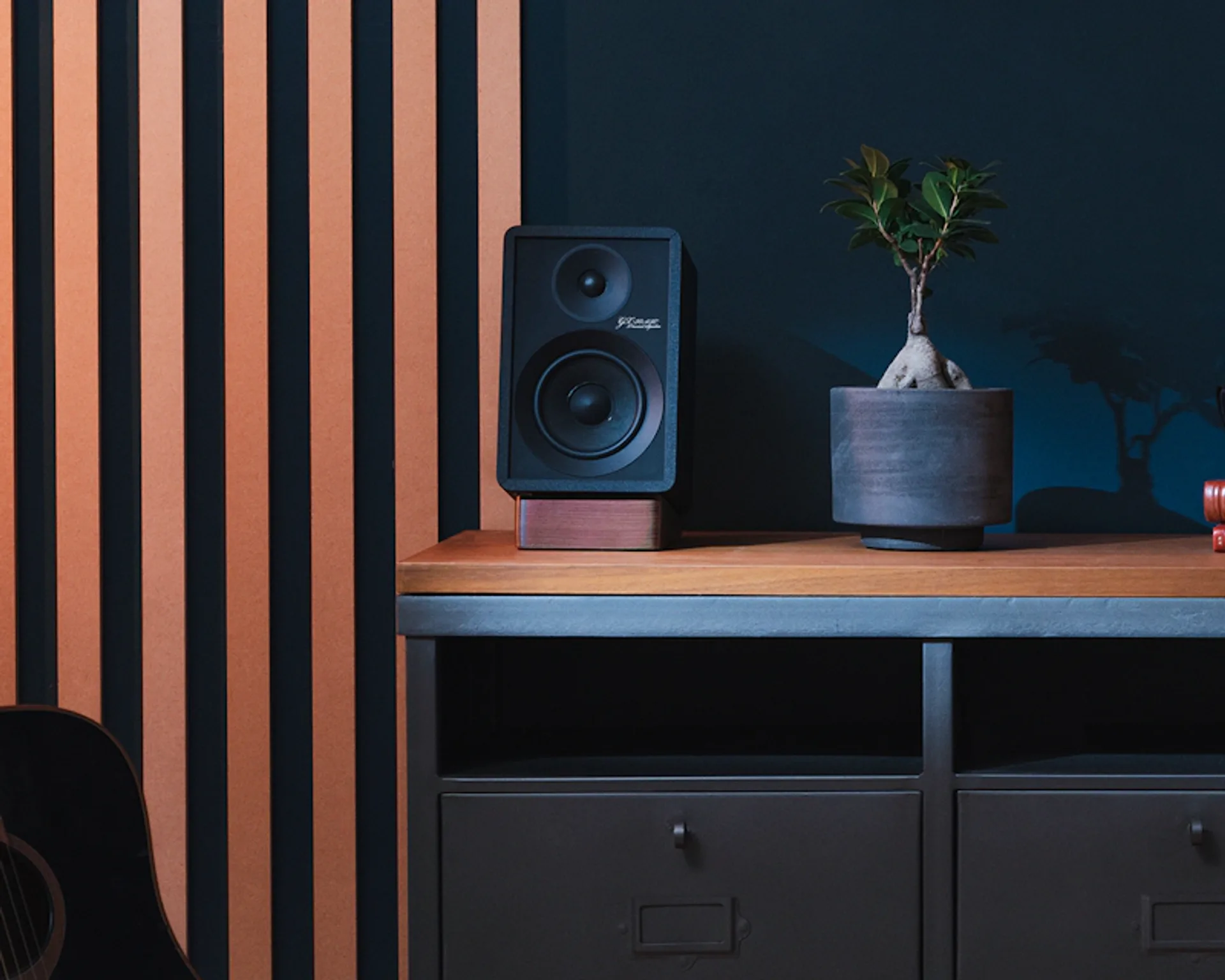 Black Onkyo Creator GX-30ARC bookshelf speaker on a wood plinth atop an industrial grey media console, navy wall, slat panel…